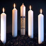 Five lit white ritual candles of varying heights on a dark textured surface.