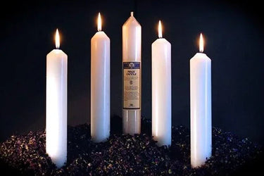 Five lit white ritual candles of varying heights on a dark textured surface.
