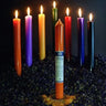 Colorful ritual spell candles in various hues arranged on dried flowers for spiritual practice.