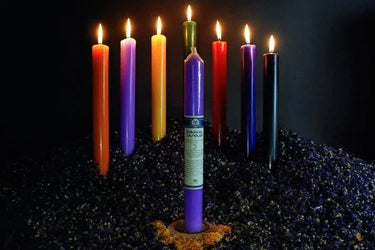 Colorful ritual spell candles lit on a bed of dried herbs for spiritual practice.