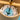 Close-up of a wooden hanging ornament or wind spinner with a blue glass disc, metal rods, and a black string inside a cylindrical wooden frame.