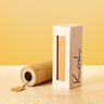 A bamboo wind instrument case standing upright next to its open cylindrical bamboo case, with a small wooden tag hanging from the open end. The white box has the brand name 'Koshi' printed vertically in black.