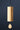 A minimalist wooden wind chime with a cylindrical body and a teardrop-shaped striker, hanging from a thin branch against a dark navy blue background.