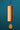 A wooden wind chime with a cylindrical body and teardrop-shaped hanging weight, suspended from a tree branch against a solid teal background.