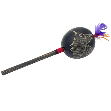 Handcrafted shamanic rattle with bird engraving and purple feathers on a wooden handle