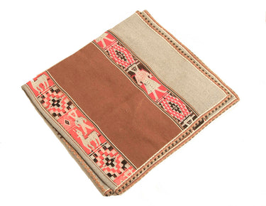 A folded woven textile, likely a blanket or throw, featuring a solid medium brown center panel, a light beige border, and a central decorative band with pink, beige, and black geometric and animal motifs.
