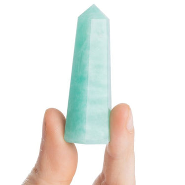 A light green translucent crystal point wand held between two fingers against a plain white background.