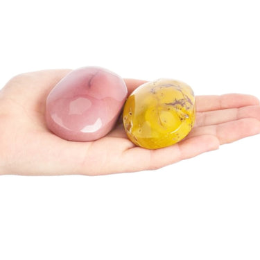 Two polished stone pendants, one pink and one yellow with dark veining, held in a person's open hand against a white background.