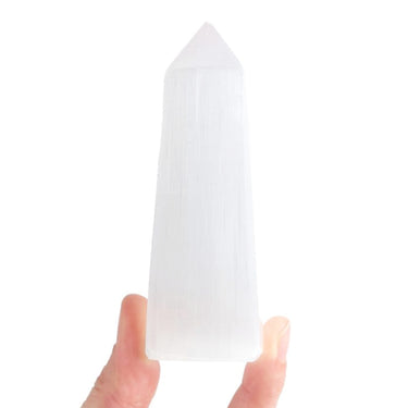 A hand holding a tall, pointed white selenite crystal tower against a plain white background.