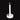 A single white taper candle in a round white holder with a crescent moon and star design, lit with a warm flame. The candle is photographed on a dark surface with dried flowers, a book, and additional white candles in the background.